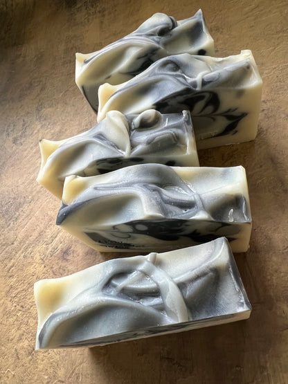Five handmade marbled soap bars with swirls of cream, gray, and black, arranged on a textured brown surface.