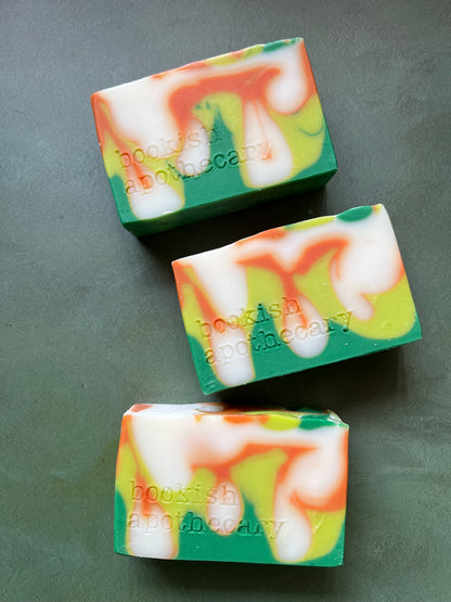 Three bars of swirled soaps comprised of orange, chartreuse and green soap stamped with bookish apothecary branding.