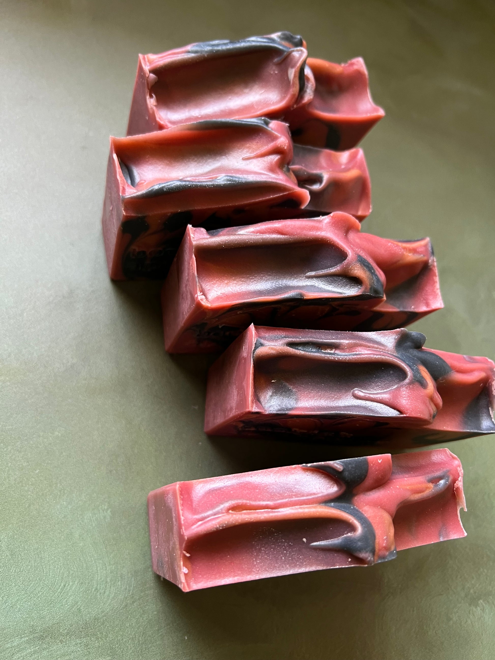 five bars of red soap with black and bronze swirls stamped with bookish apothecary branding.