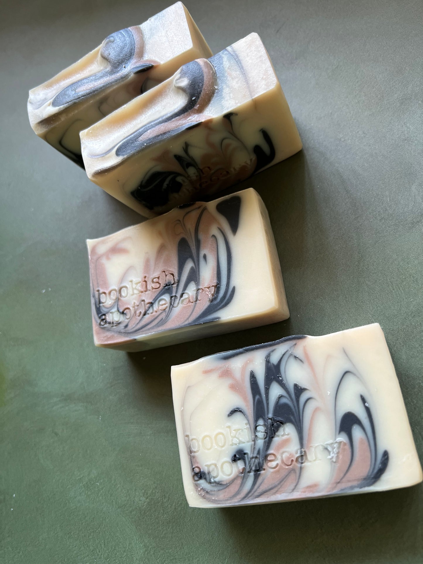four bars of white soap with black and tan swirls stamped with bookish apothecary branding.