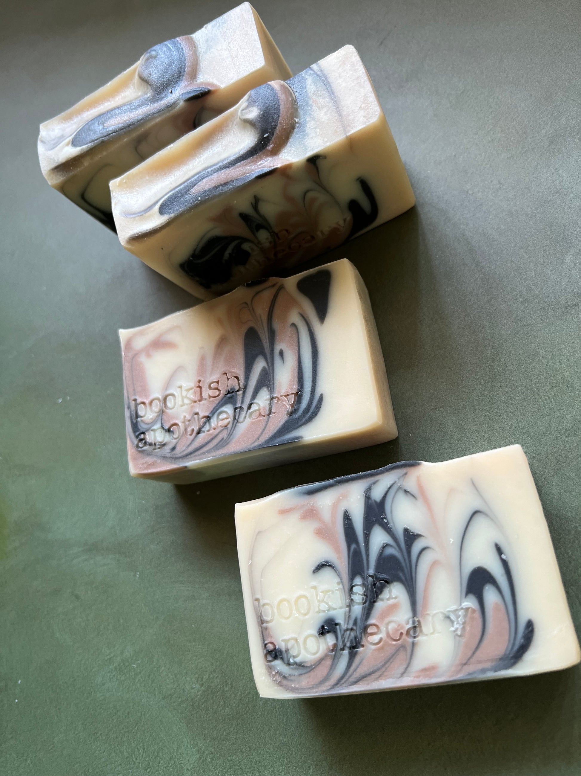 four bars of white soap with black and tan swirls stamped with bookish apothecary branding.