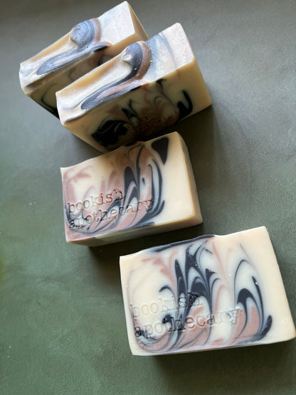 four bars of white soap with black and tan swirls stamped with bookish apothecary branding.