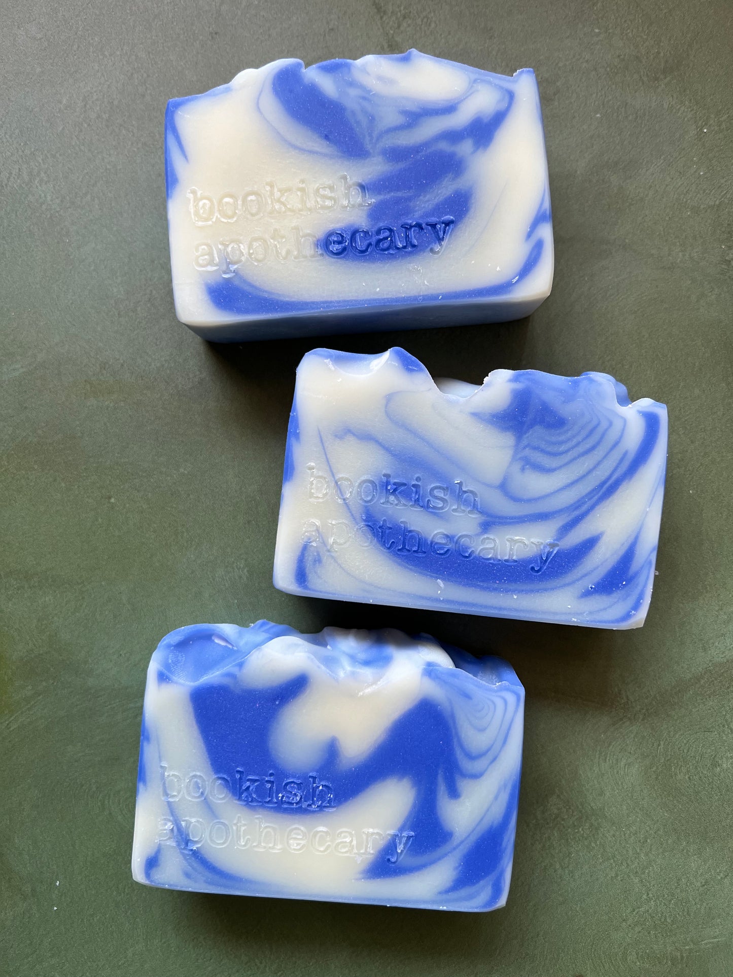 Three bars of blue and white swirled soaps stamped with bookish apothecary branding.