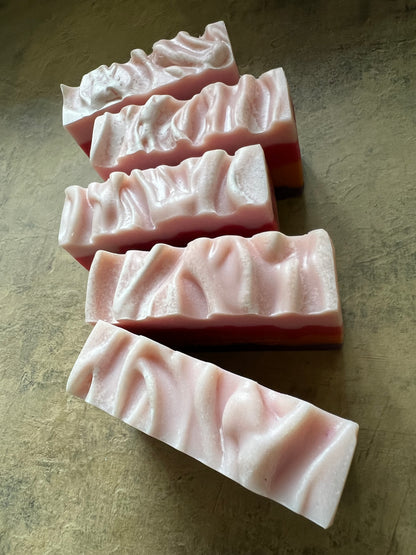 Five rectangular bars of handmade soap with a wavy, textured surface, arranged diagonally on a textured gray surface.