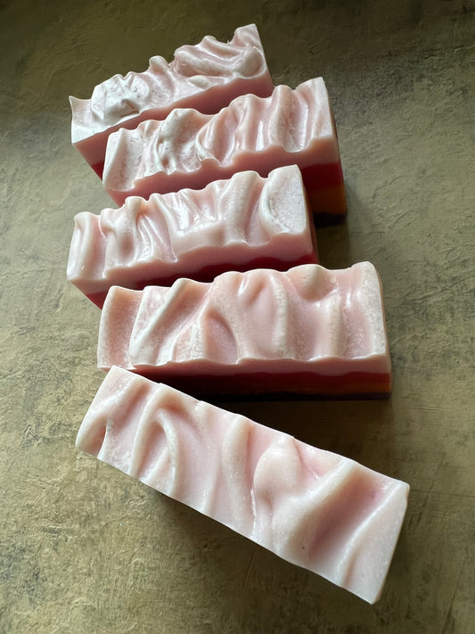 Five rectangular bars of handmade soap with a wavy, textured surface, arranged diagonally on a textured gray surface.