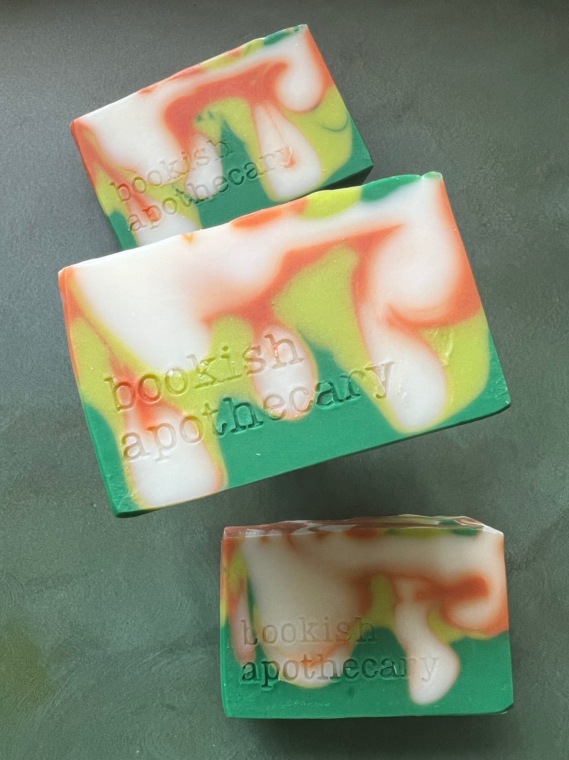Three bars of swirled soaps comprised of orange, chartreuse and green soap stamped with bookish apothecary branding.