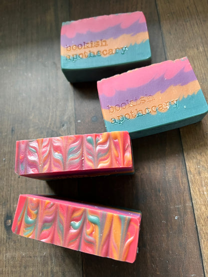 Colorful soap bars with 'bookish apothecary' branding on a wooden surface