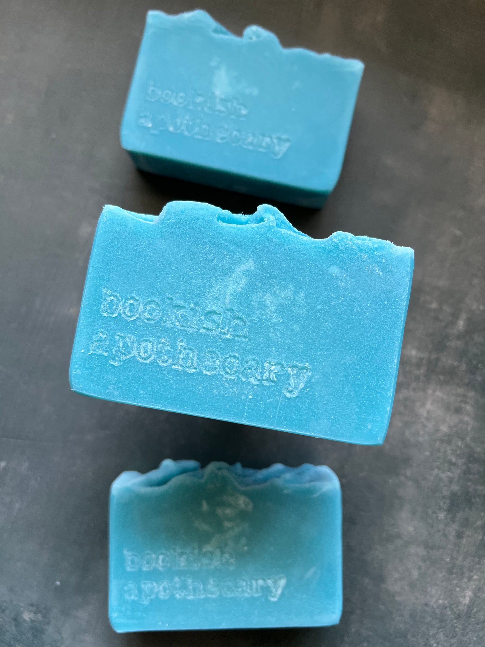 Three blue soap bars with 'bookish Apothecary' branding on a gray surface
