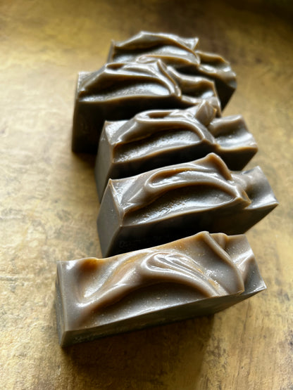 Five rectangular bars of handmade soap with textured, swirled tops, arranged diagonally on a rustic, warm brown surface.