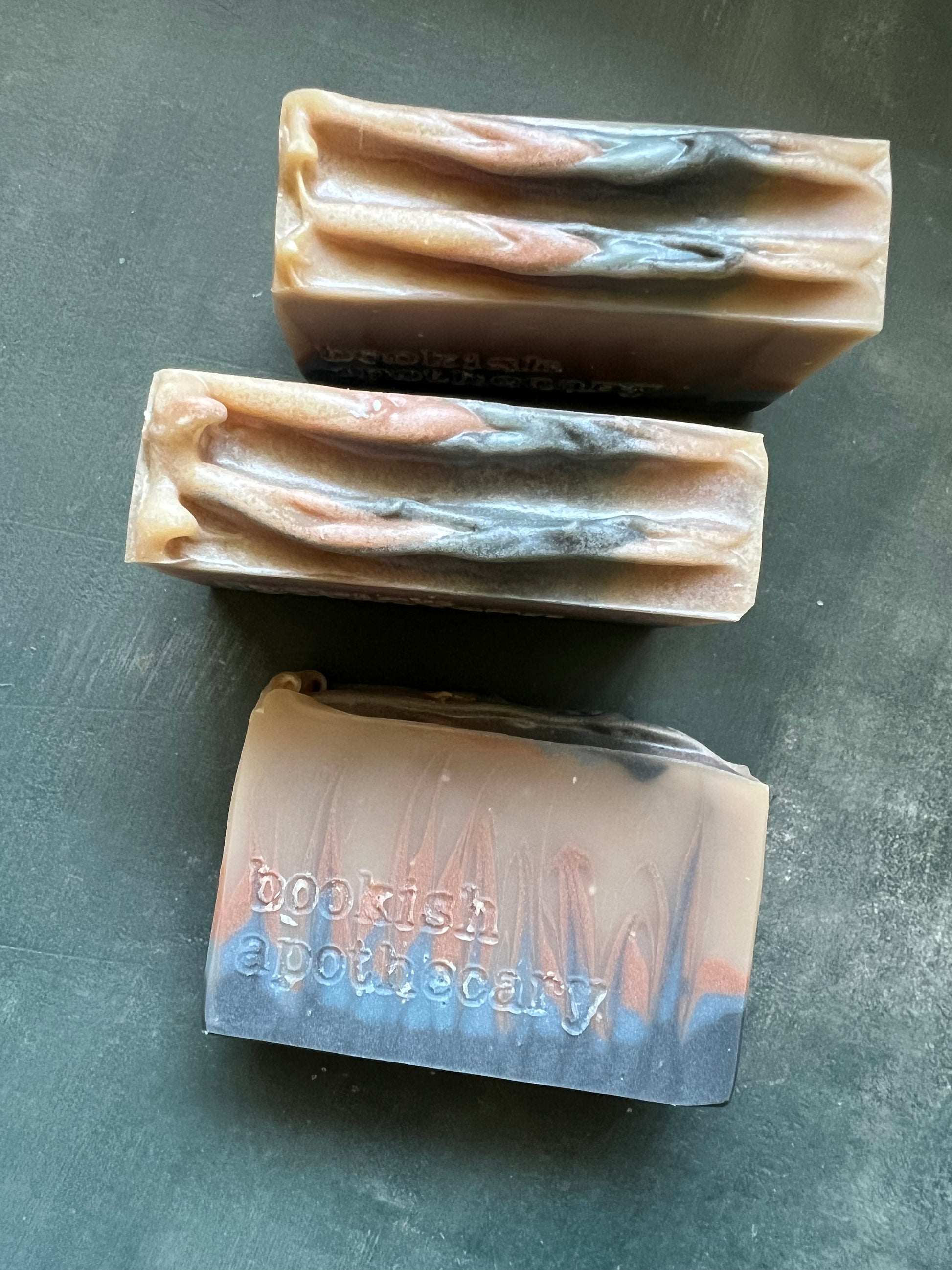 Three bars of soap on a dark surface with 'bookish apothecary' branding.