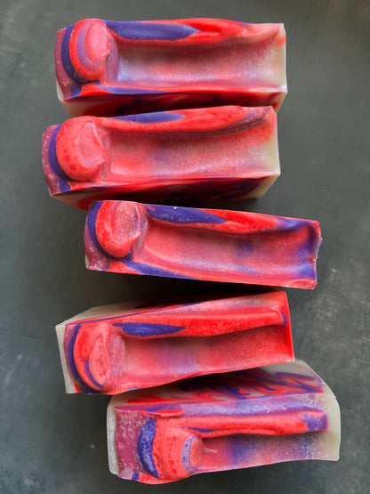 Five bars of red and purple soap arranged on a dark surface