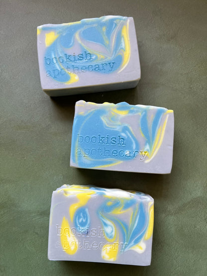 Three bars of gray soap with blue, yellow and white swirls stamped with bookish apothecary branding.