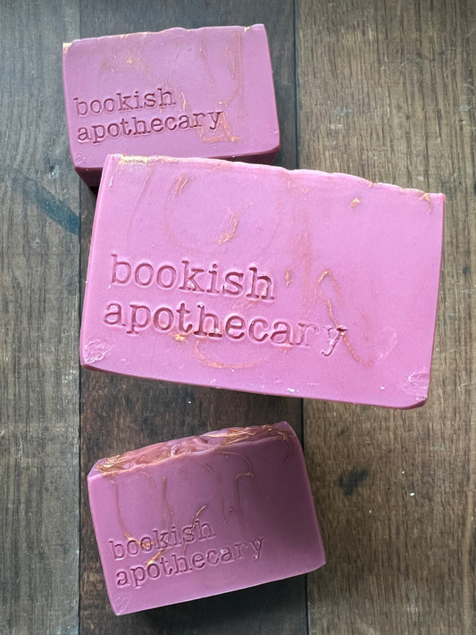 Three bars of pink soap with 'bookish apothecary' branding on a wooden surface.