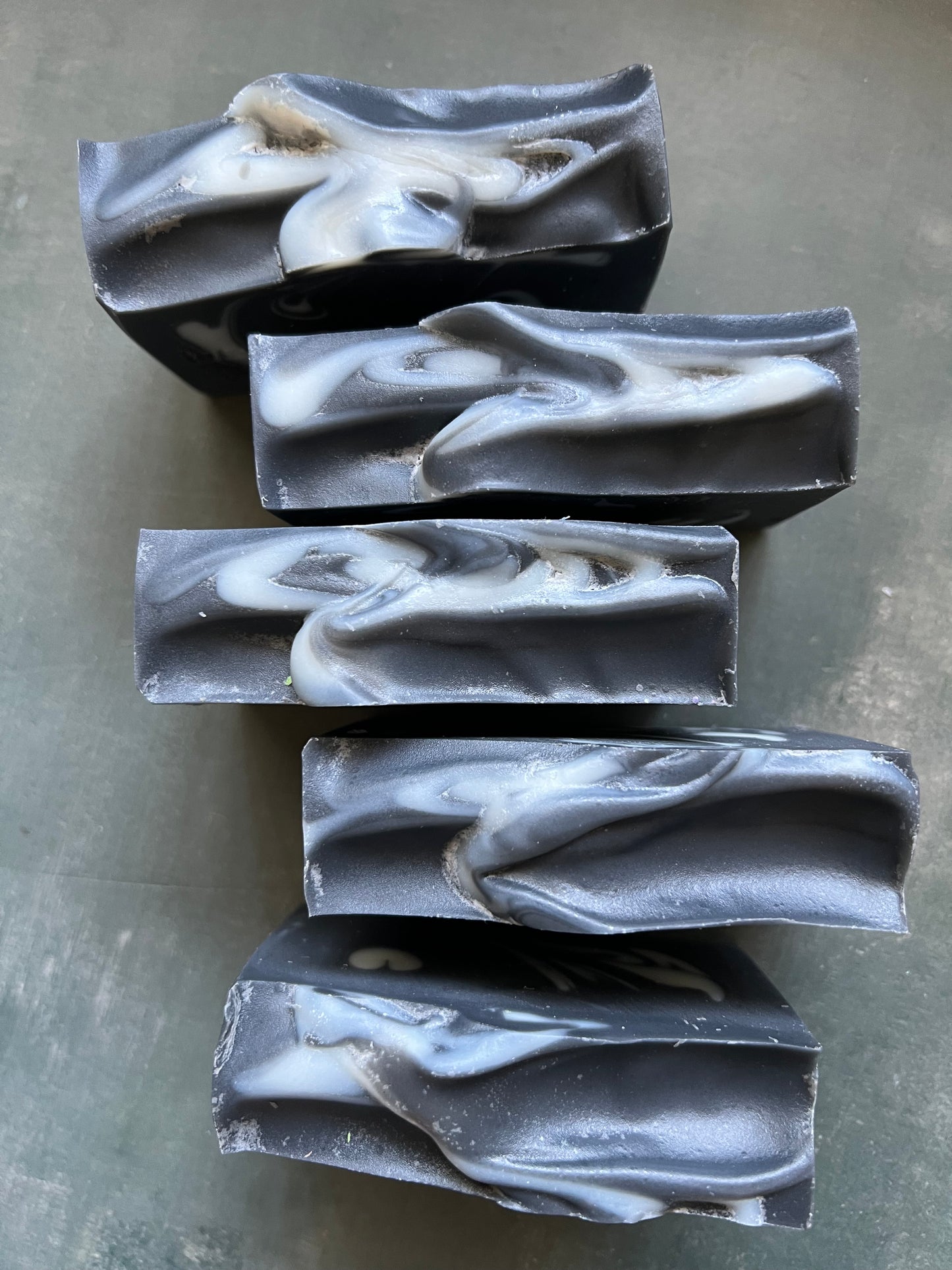 Five bars of black and white marbled soap on a gray surface