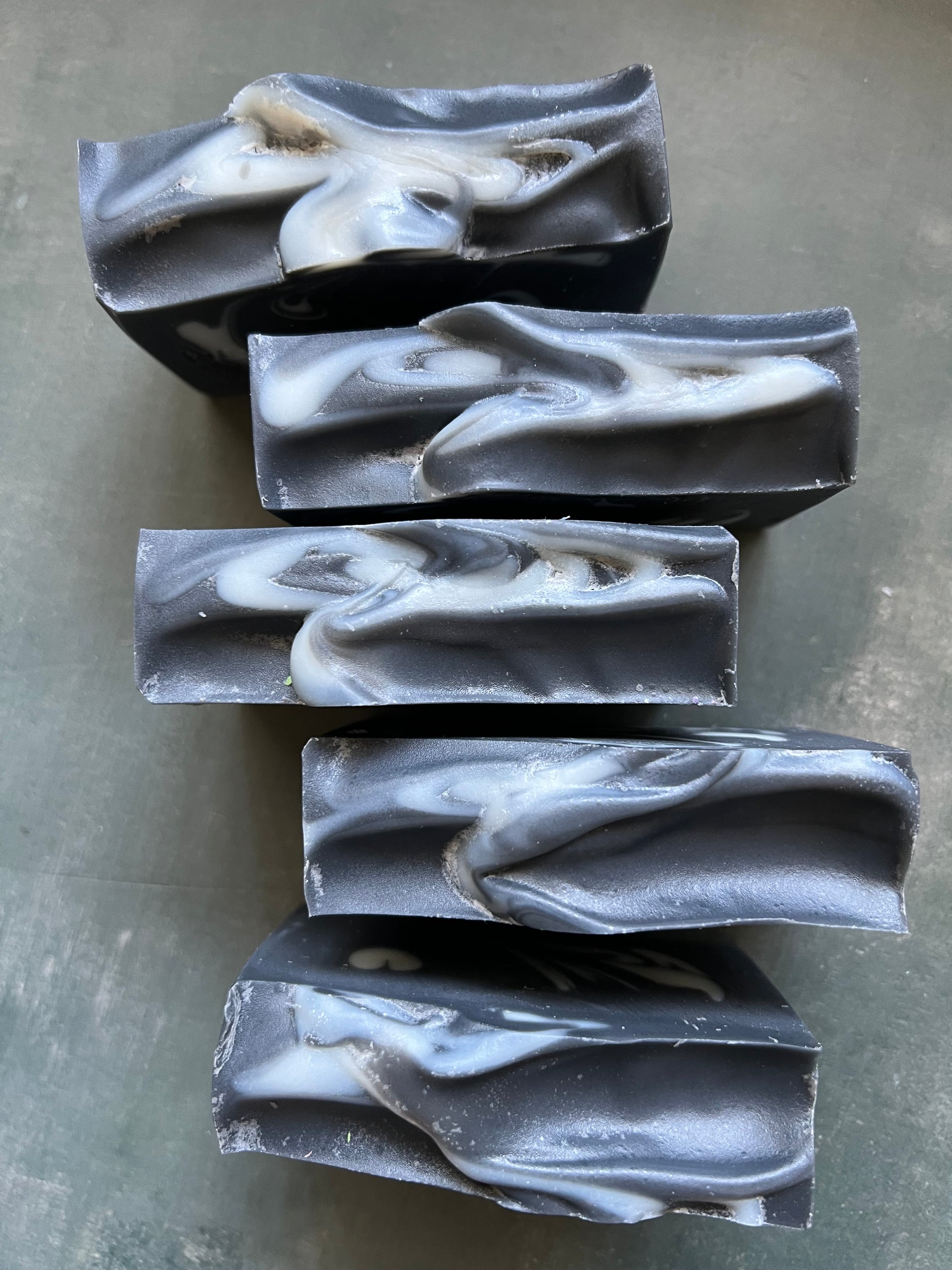 Five bars of black and white marbled soap on a gray surface