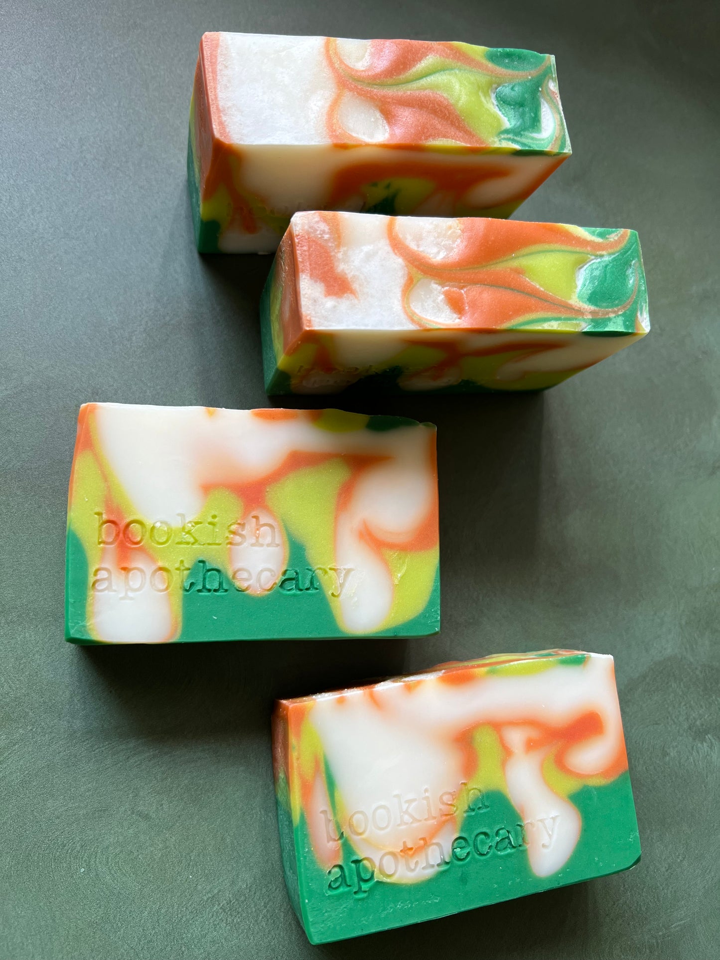 four bars of swirled soaps comprised of orange, chartreuse and green soap stamped with bookish apothecary branding.