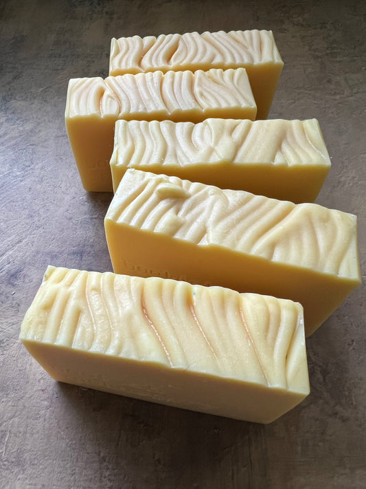 Four rectangular bars of handmade soap with a wavy, textured pattern, shown on a dark gray textured surface.