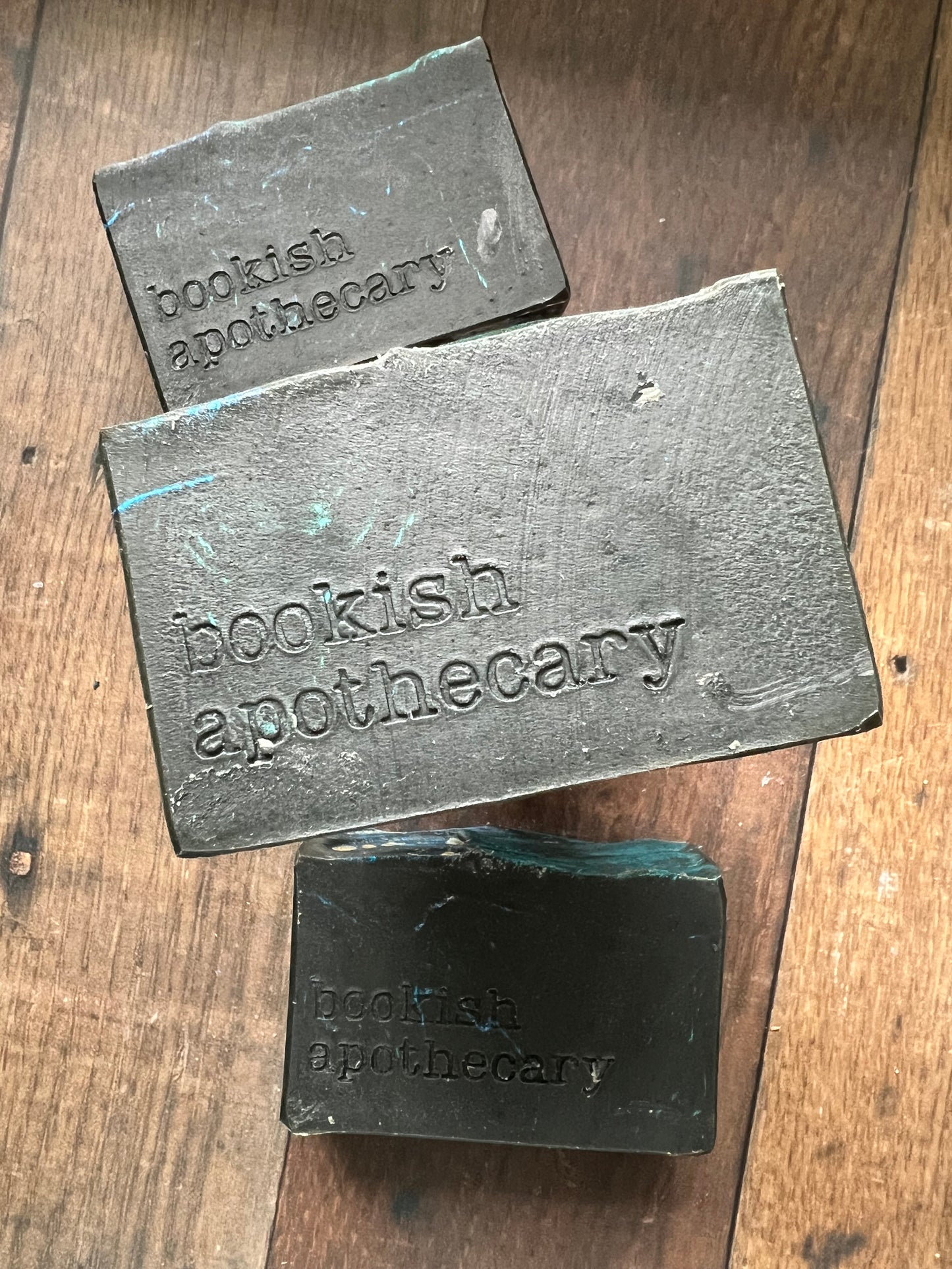 Three bars of black soap from 'bookish apothecary' on a wooden surface