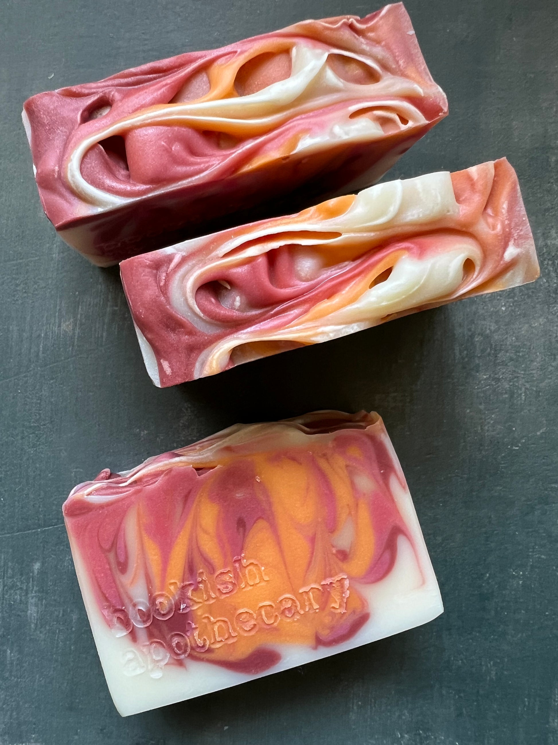 Three bars of swirled soap on a dark surface, with 'bookish apothecary' branding.