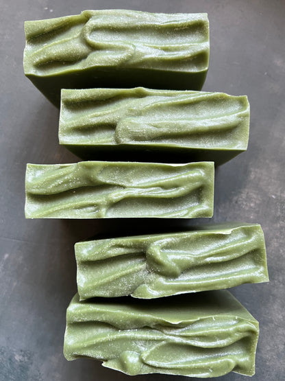 Five green soap bars with a textured surface on a dark gray background