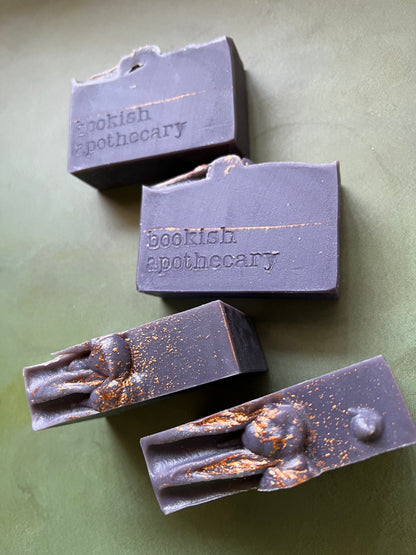 Four bars of dark purple soap stamped with bookish apothecary branding.