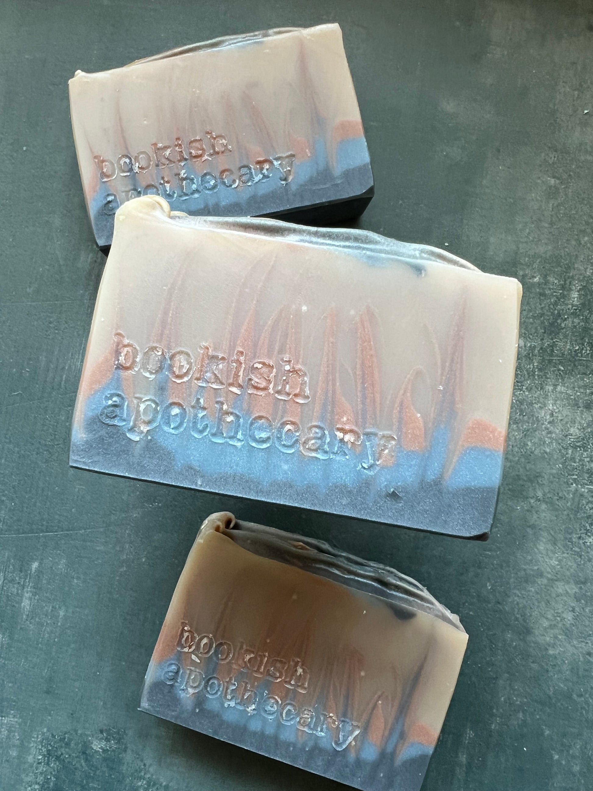 Three bars of soap with 'bookish Apothecary' branding on a gray surface.