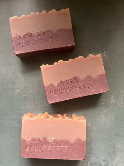 Three bars of soap with 'bookish apothecary' branding on a dark surface