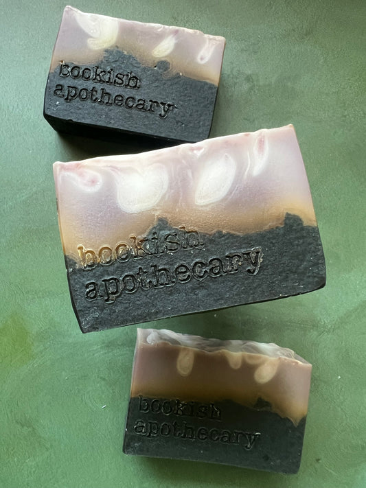 Three bars of  soap with a tan top and black bottom stamped with bookish apothecary branding.