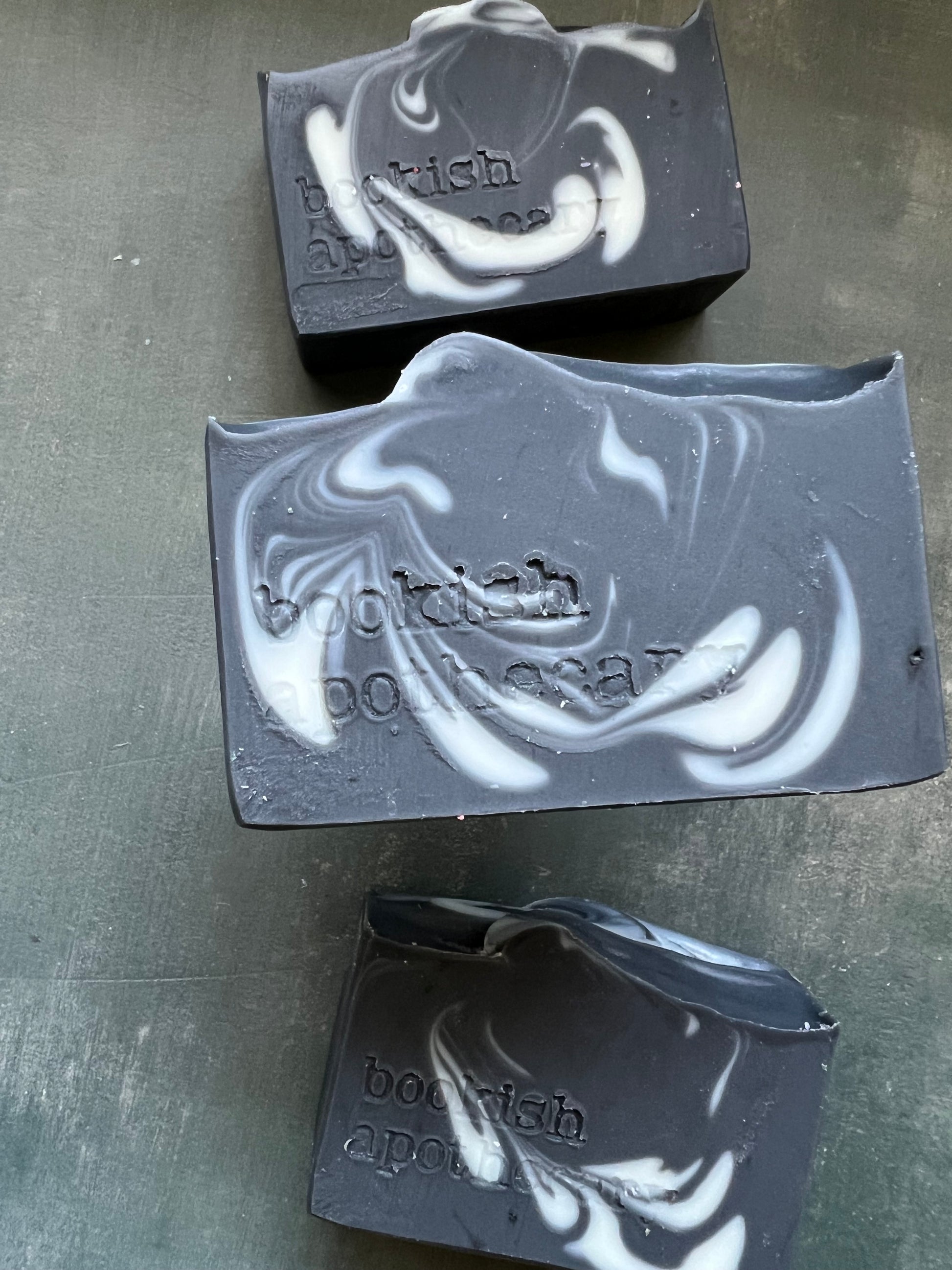 Three bars of black and white marbled soap on a gray surface