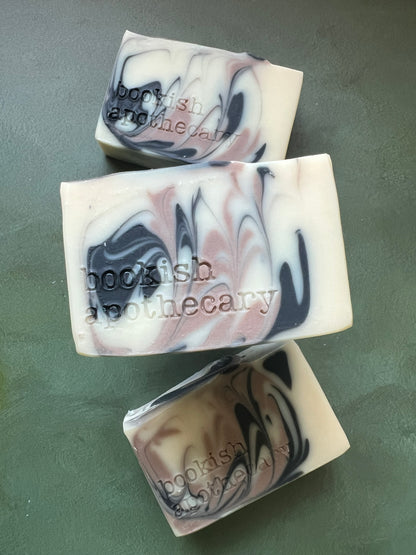 Three bars of white soap with black and tan swirls stamped with bookish apothecary branding.