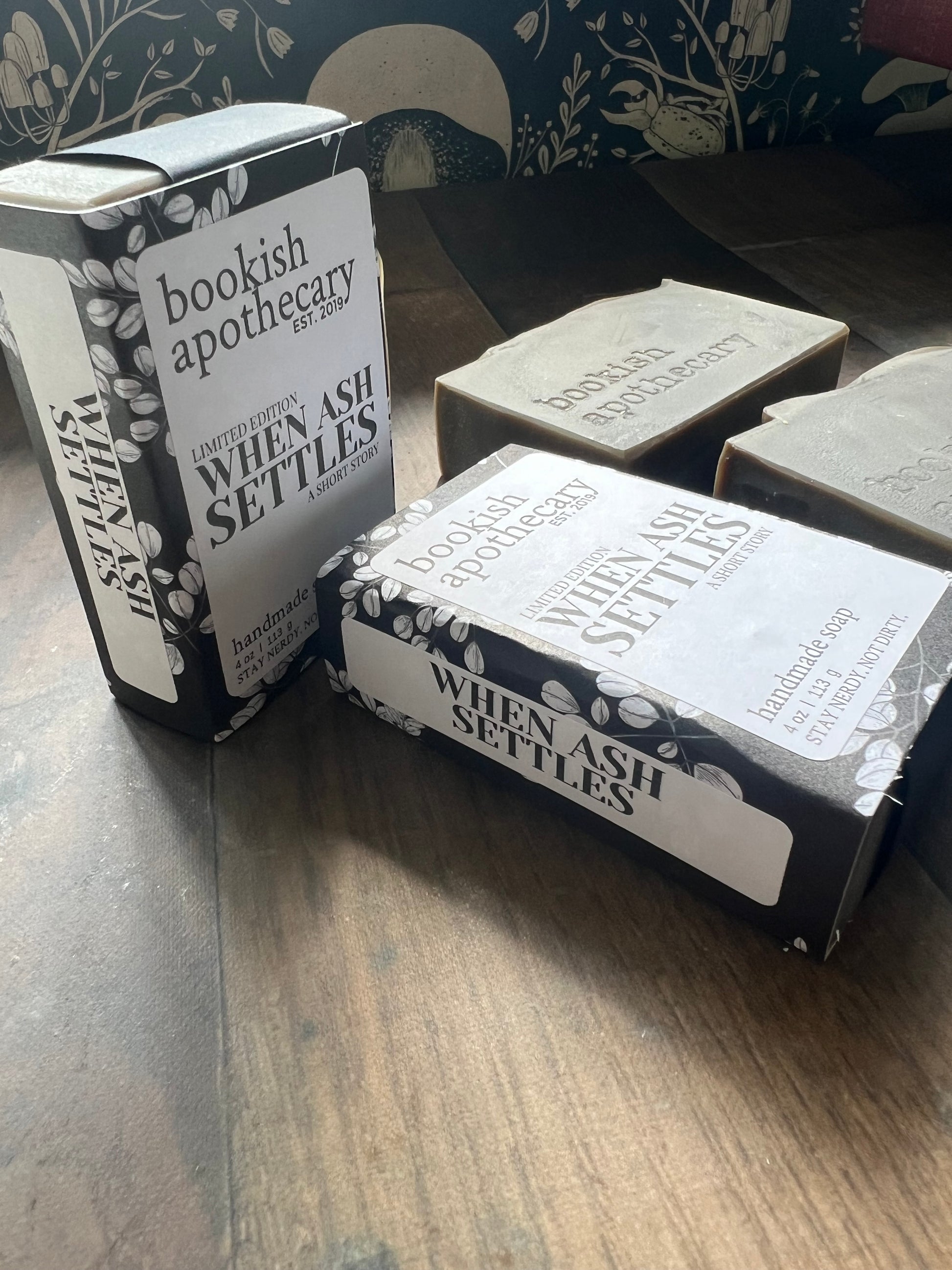 Two 'When Ash Settles' bookish apothecary soap and boxes on a wooden surface