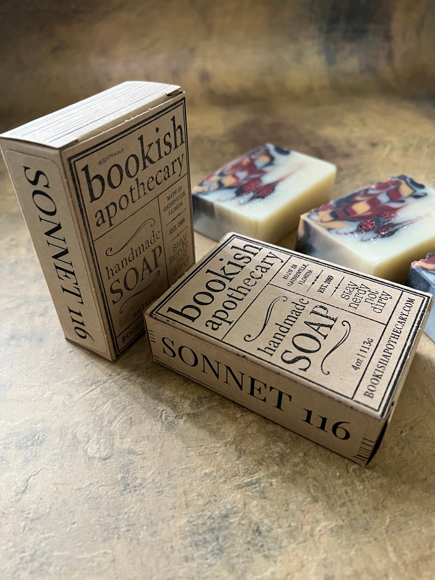 A boxed soap product labeled 'Bookish Apothecary SOAP' and 'SONNET 116' shown with two matching paperboard boxes and one visible soap bar in the background, arranged on a textured beige surface.