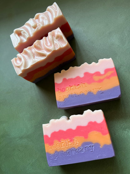 four bars of soap with layers of pink, red, orange and purple stamped with bookish apothecary branding.