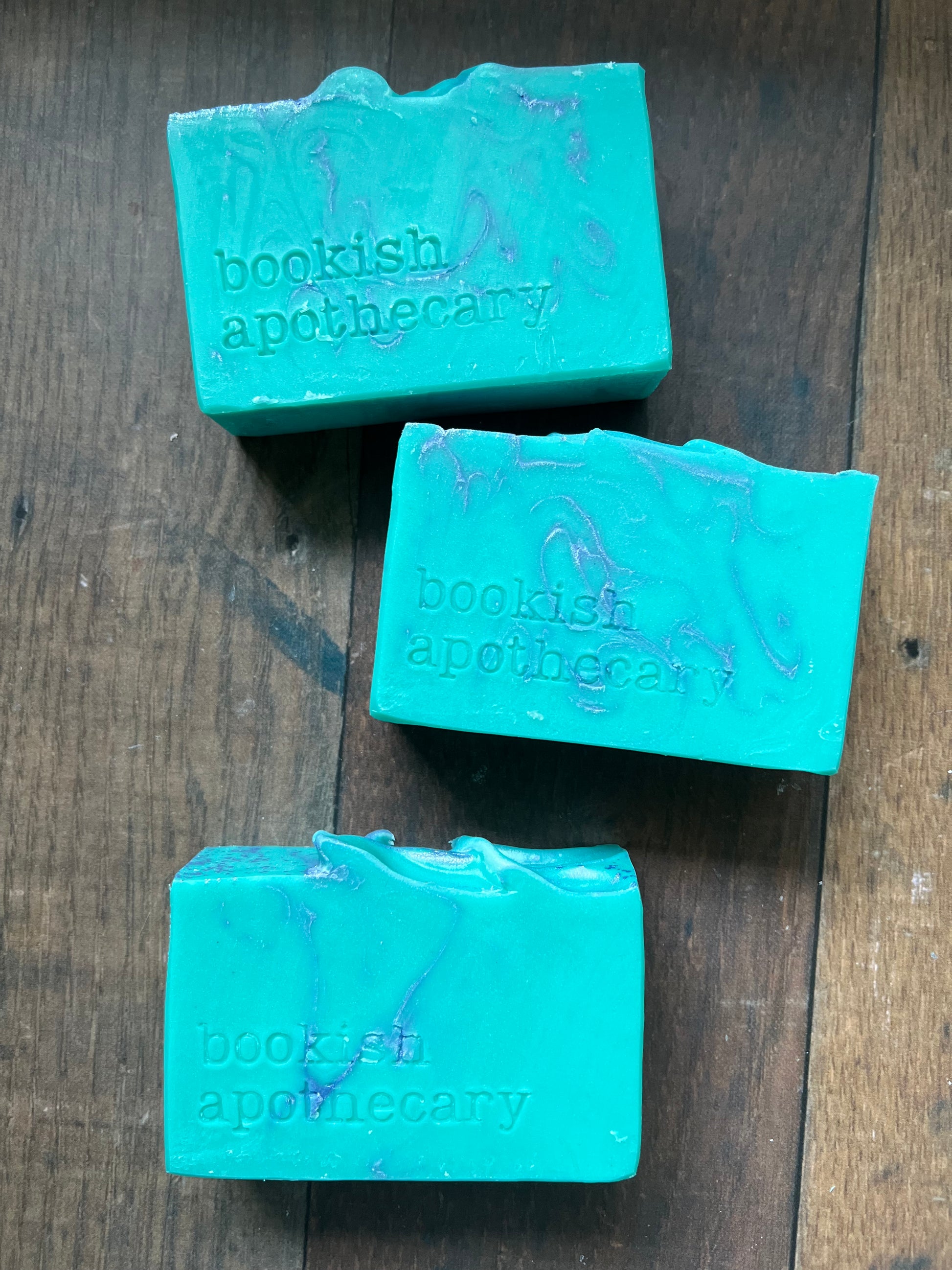 Three bars of teal soap with 'bookish apothecary' branding on a wooden surface.