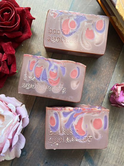 Three bars of soap with marbled design on a wooden surface with flowers.