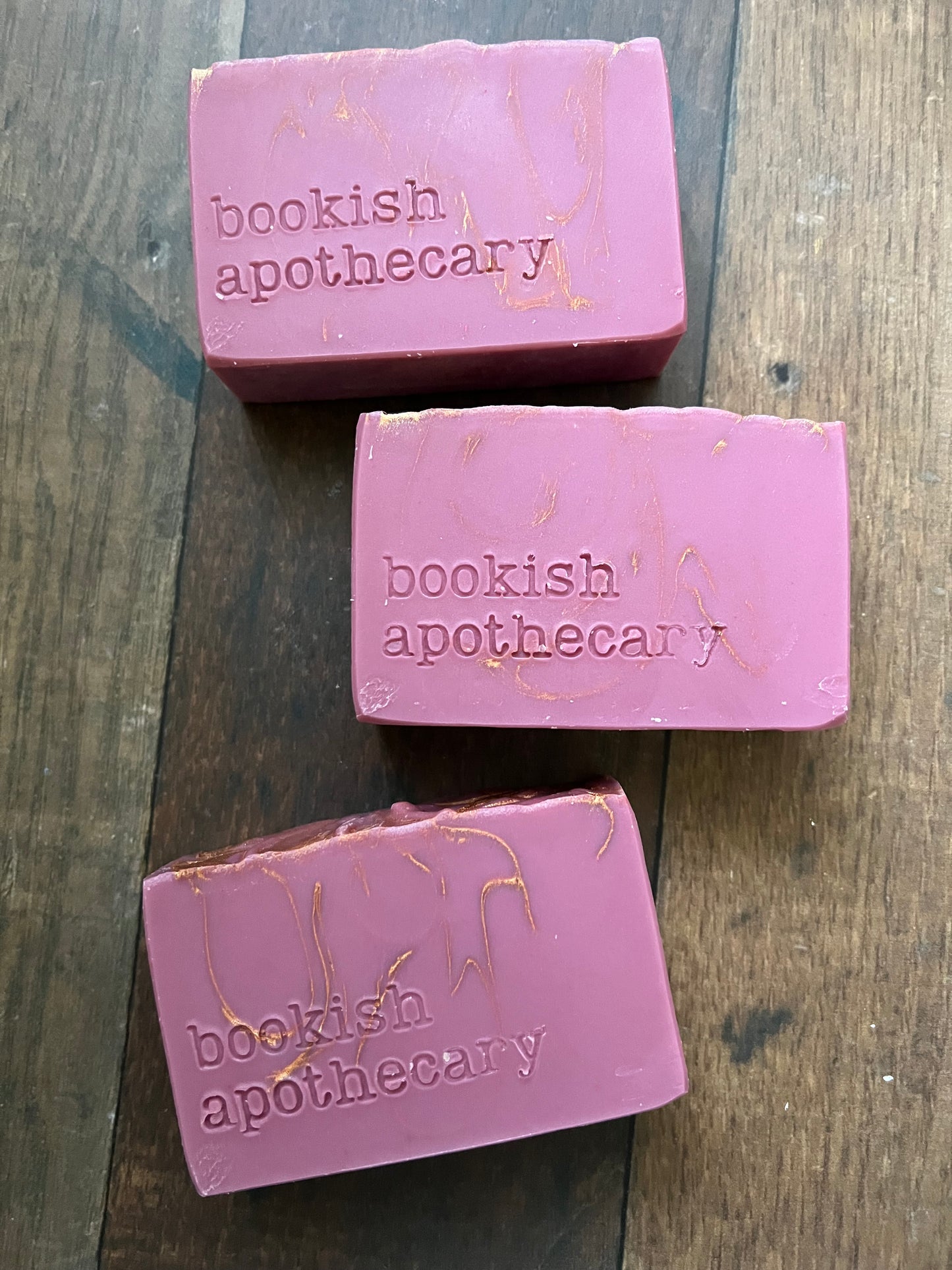 Three bars of pink soap with 'bookish apothecary' branding on a wooden surface.