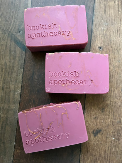 Three bars of pink soap with 'bookish apothecary' branding on a wooden surface.