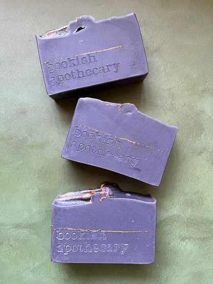 Three bars of dark purple soap stamped with bookish apothecary branding.