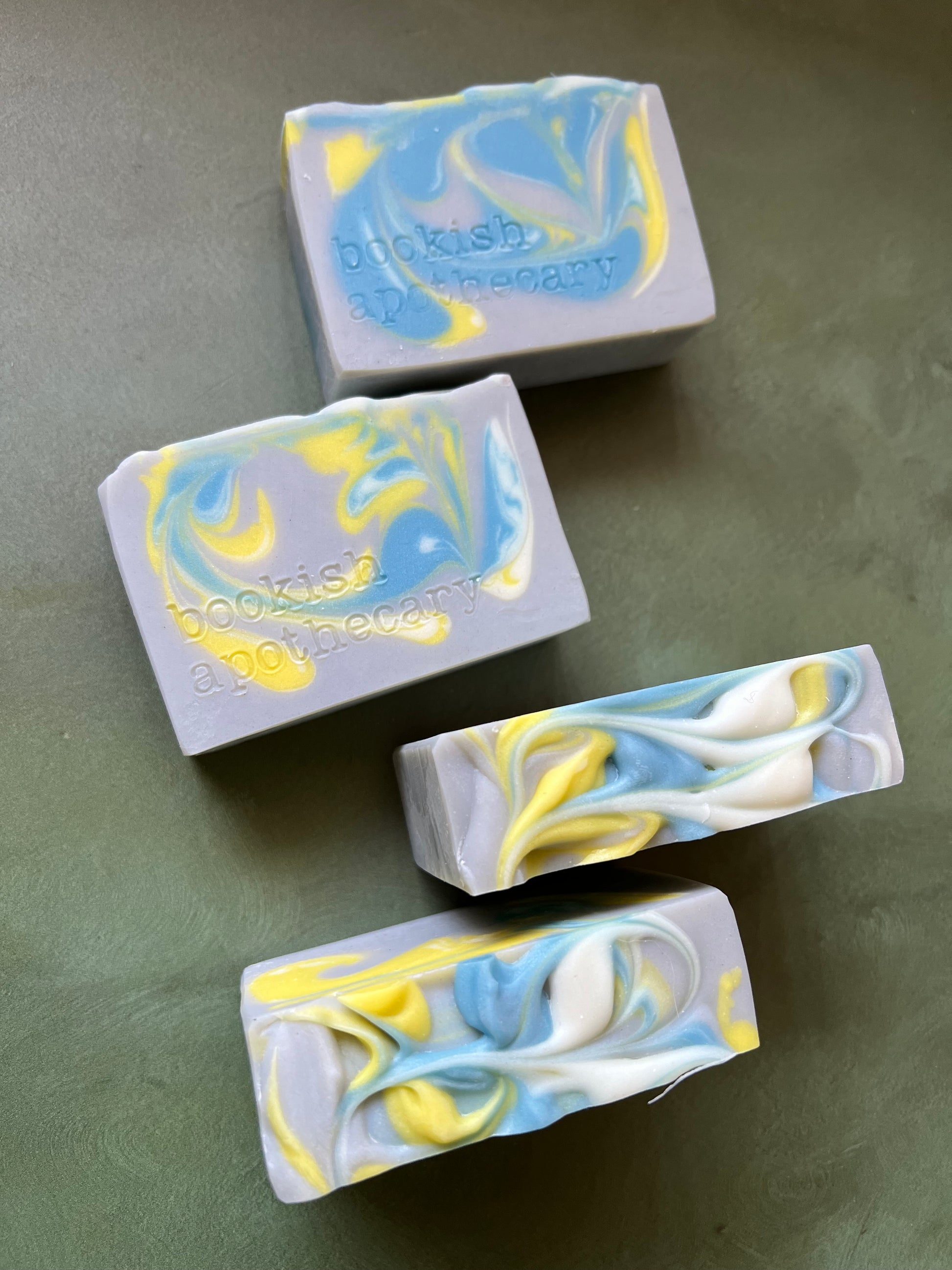 four bars of gray soap with blue, yellow and white swirls stamped with bookish apothecary branding.