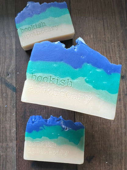 Four bars of soap with gradient colors and 'Bookish apothecary' branding on a wooden surface.