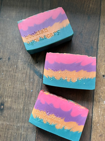 Three colorful soap bars with 'bookish apothecary' branding on a wooden surface.