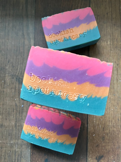 Three colorful soap bars with 'BooKish Apothecary' branding on a wooden surface.