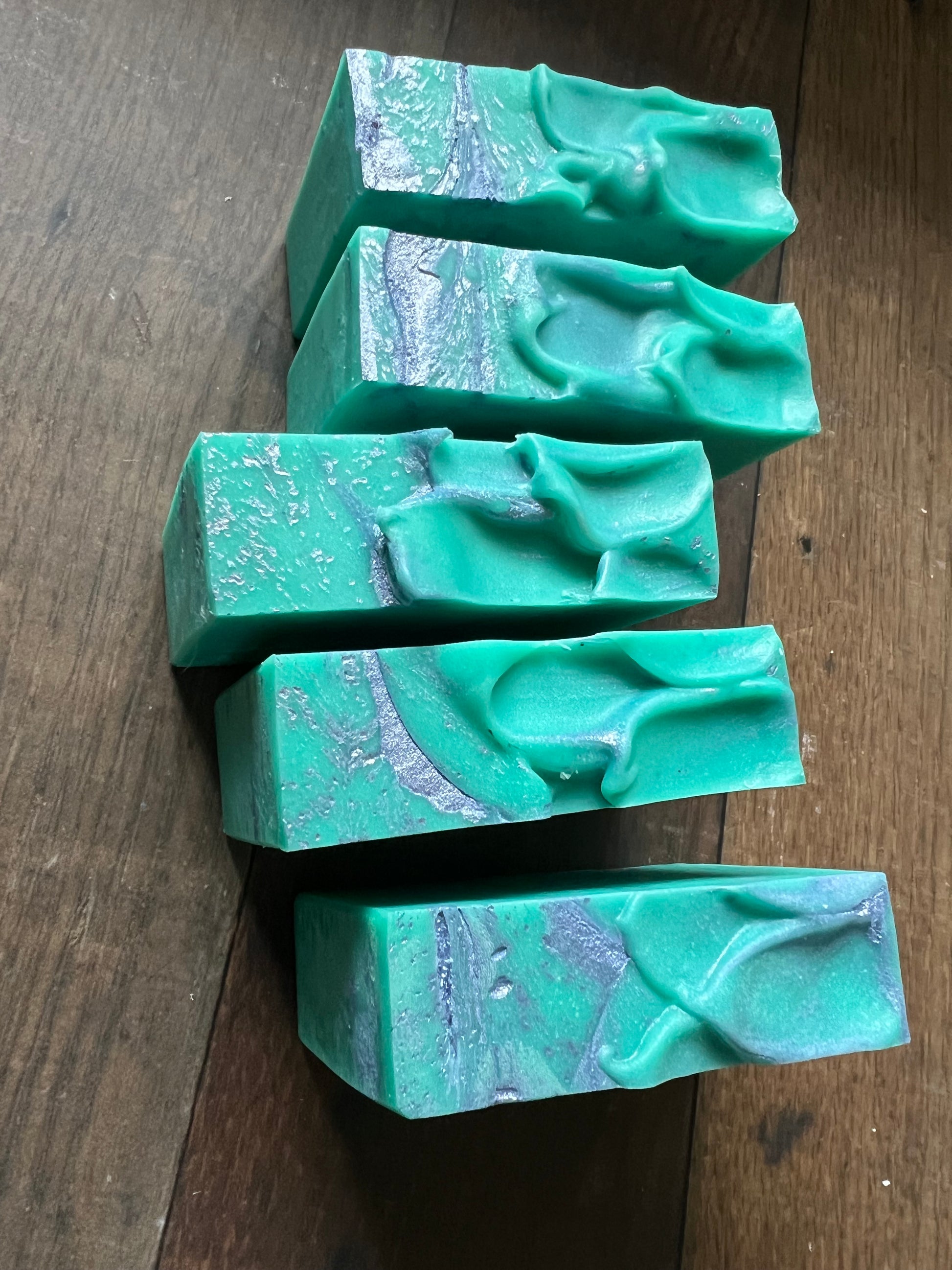 Five green soap bars with marbled patterns on a wooden surface