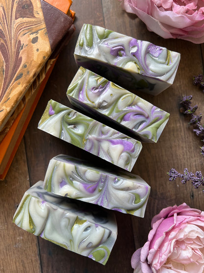 Five swirled soap bars on a wooden surface with flowers and books in the background