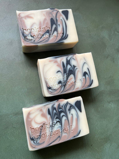 Three bars of white soap with black and tan swirls stamped with bookish apothecary branding.