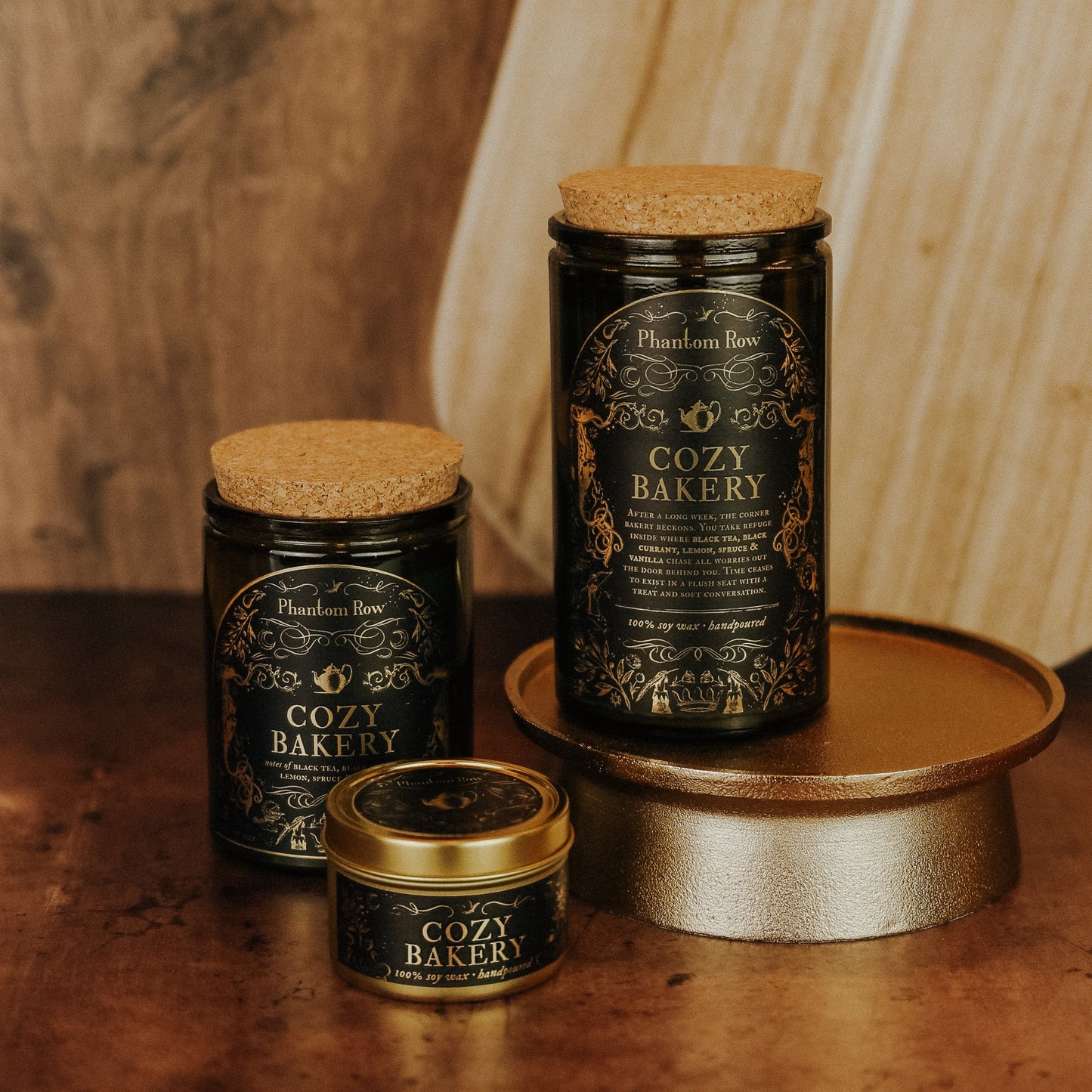 Three 'Cozy Bakery' candles from Phantom Row on a wooden surface with a warm background.