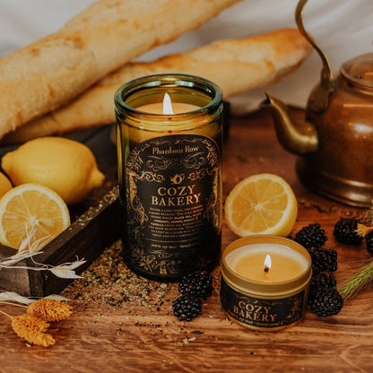 Candle in a glass bottle labeled 'Cozy Bakery' on a wooden surface with lemons and bread.
