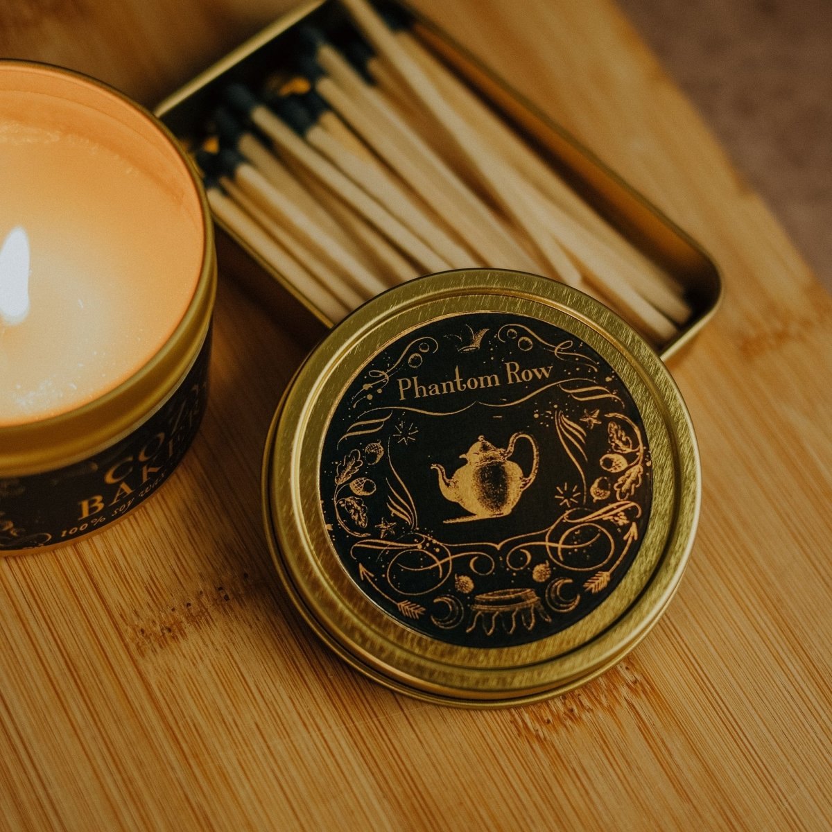 Matchbox and candle on a wooden surface with 'Phantom Row' branding.