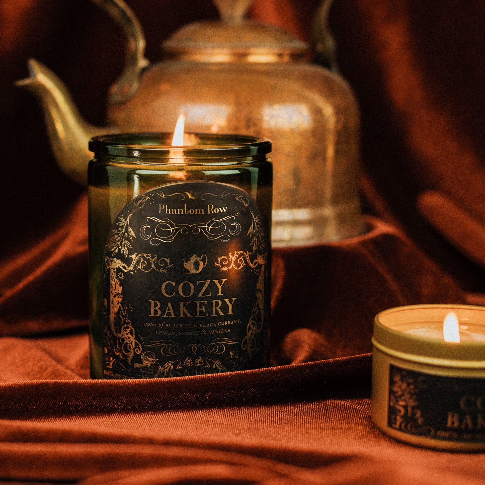 Candle labeled 'Cozy Bakery' with decorative design on a warm-toned fabric background.