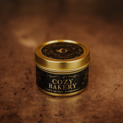 Candle in a 'Cozy Bakery' tin with a gold lid on a brown background